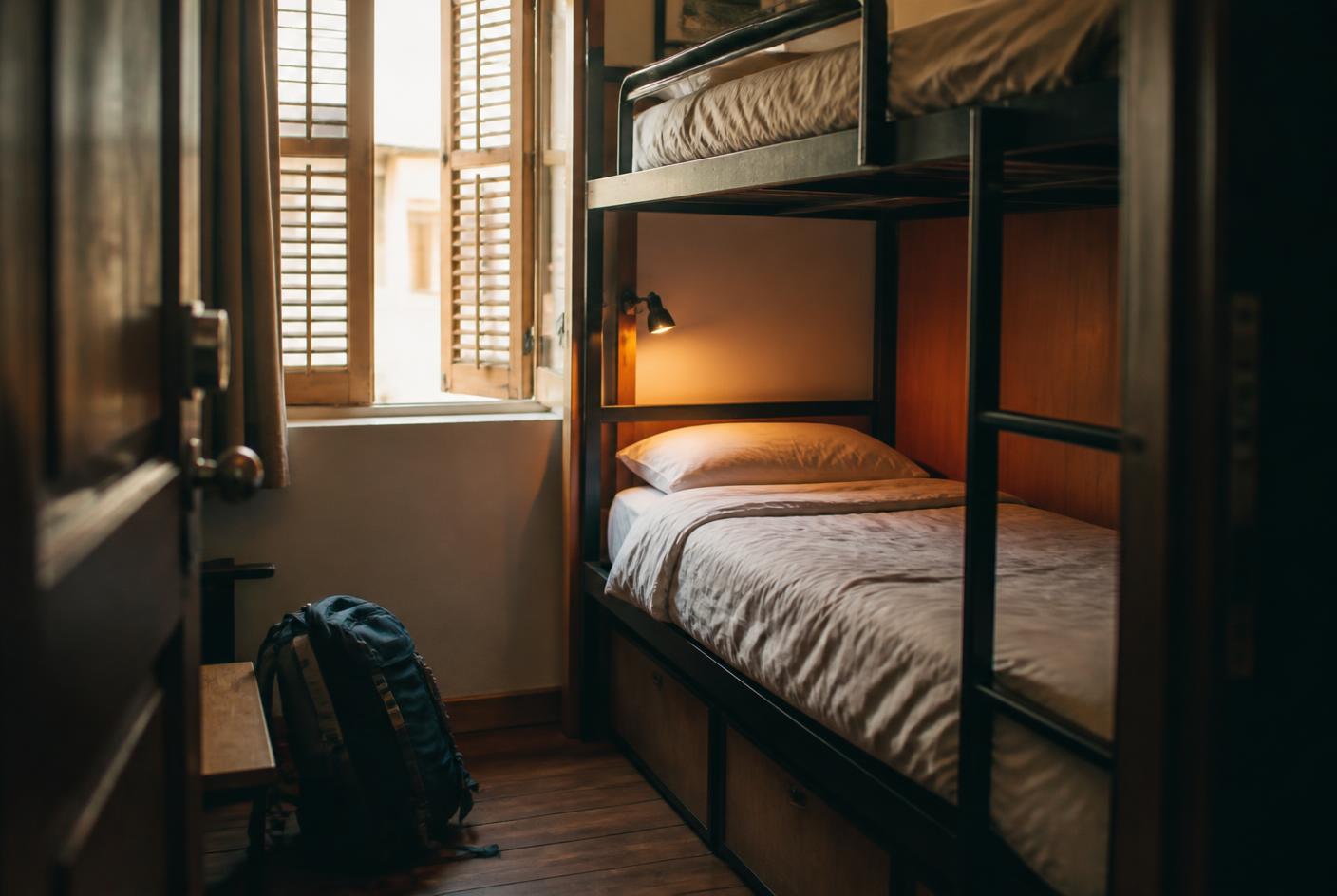 A hostel dorm bunk bed with morning light through the shutters